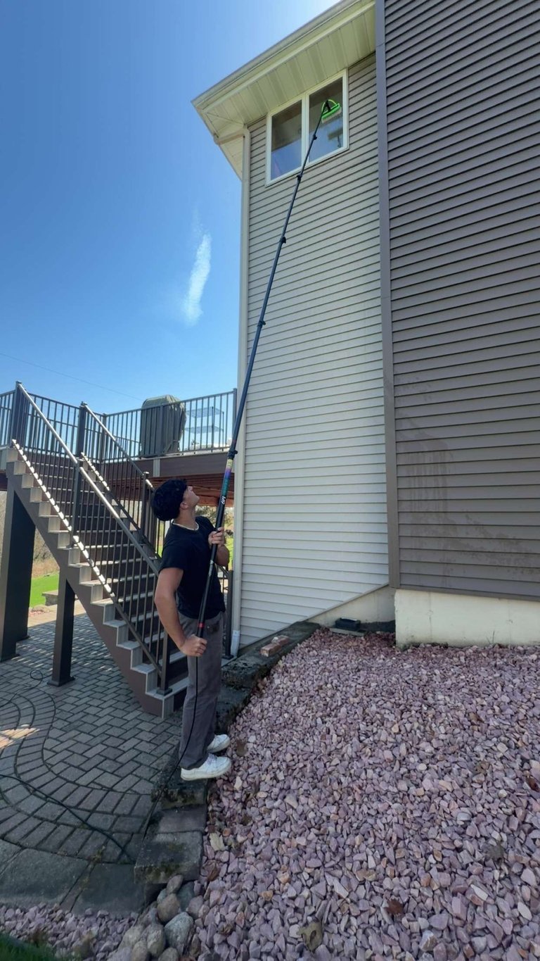 Worker in safety gear climbing an extension ladder against a light-colored wooden building with metal stairs nearby