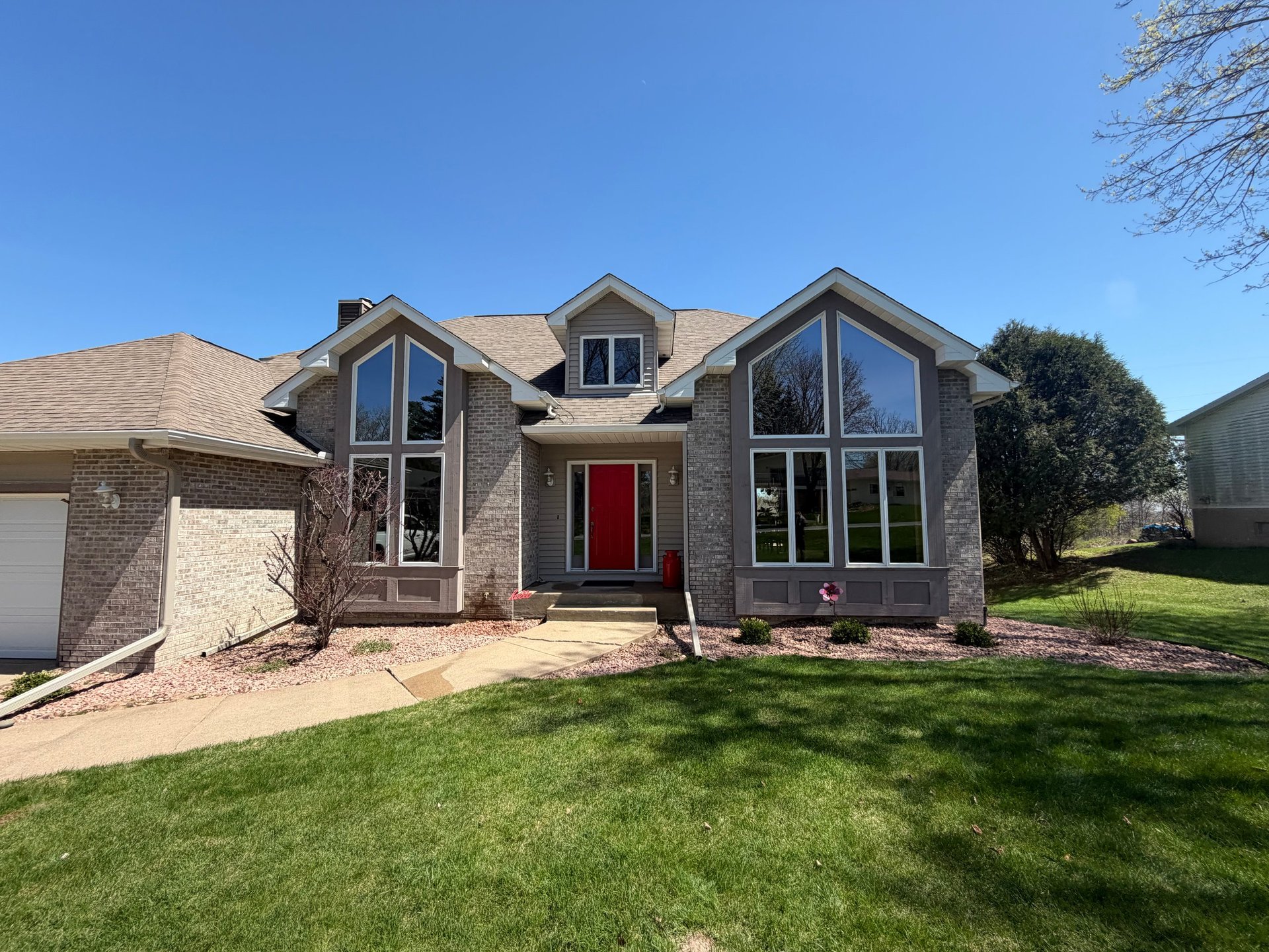 Brick and stone residential home with red front door, large windows, and well-maintained lawn on a clear day